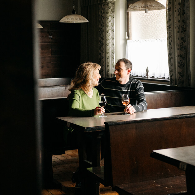 Herr und Frau Steiger sitzen im Heurigen an einem Tisch und trinken Rosé Wein