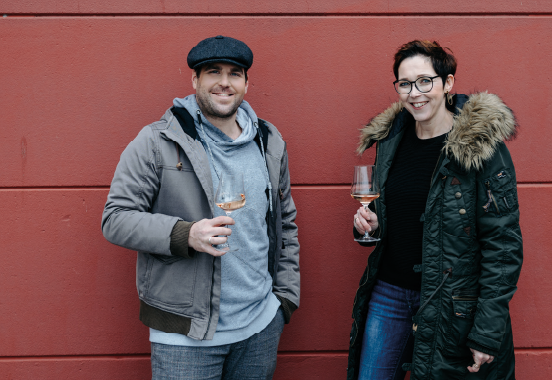 Herr Kurz und Frau Schandl mit einem Weinglas vor einer roten Wand